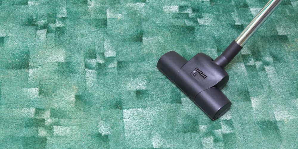 Vacuum cleaner nozzle being used to clean a textured green carpet floor